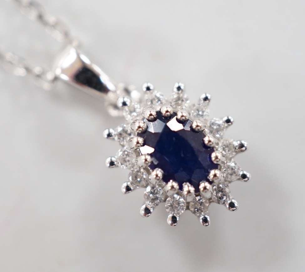 A modern 9ct white gold, sapphire and diamond set oval cluster pendant, overall 15mm,on a modern 9ct white gold chain, 40cm, gross weight 2.8 grams.